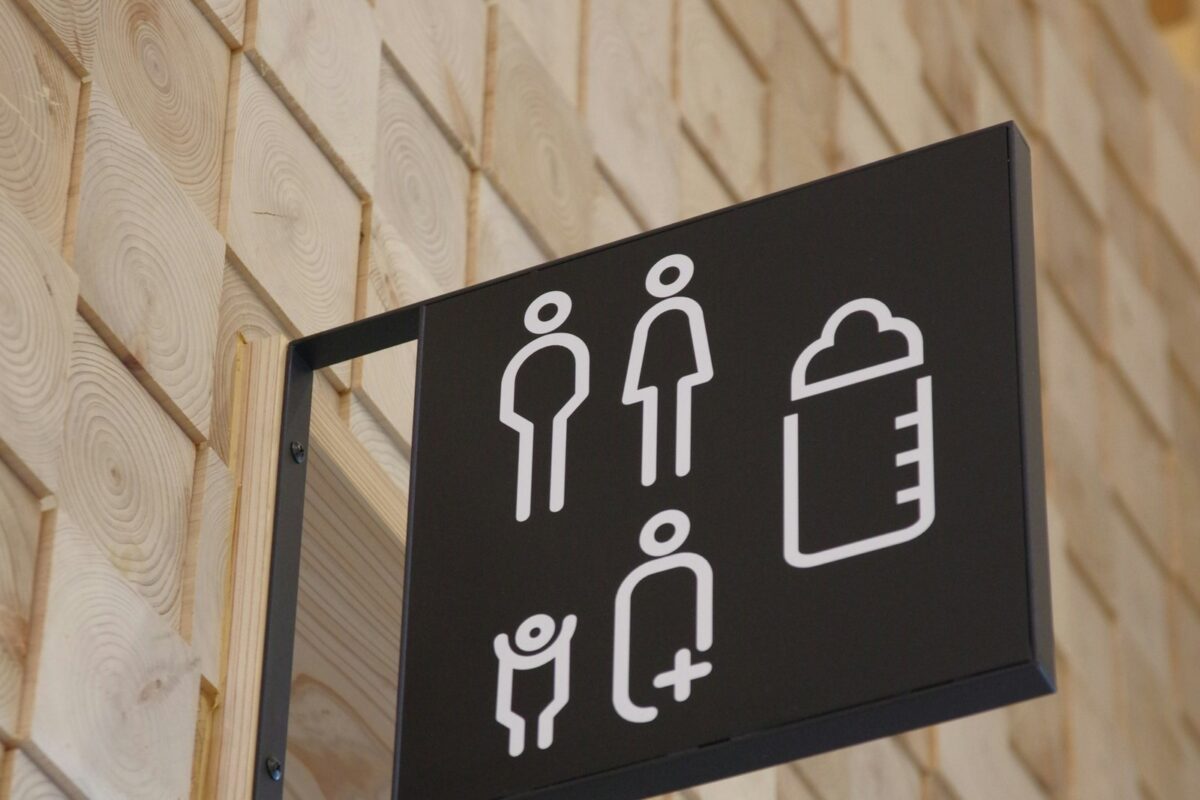 Dark restroom sign with white pictograms for adults, family, and baby changing mounted on a light wood wall
