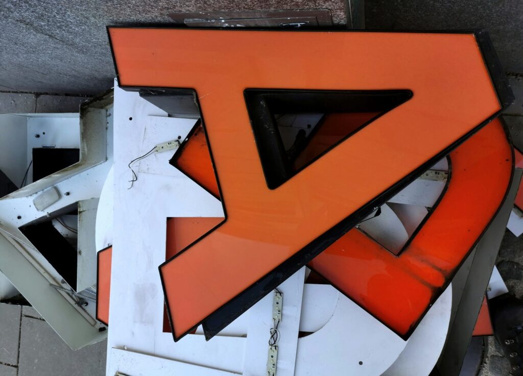 Disassembled orange channel letter sign faces and returns stacked together