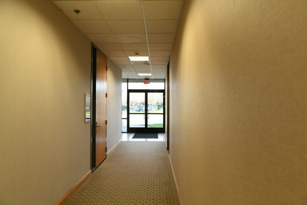 Long carpeted hallway with beige walls leading to a glass exit door