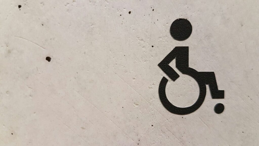 Black wheelchair accessibility symbol painted on a light concrete wall