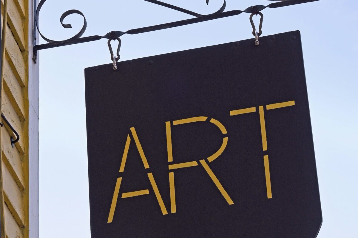 Black projecting blade sign hanging from a decorative metal bracket on the side of a building