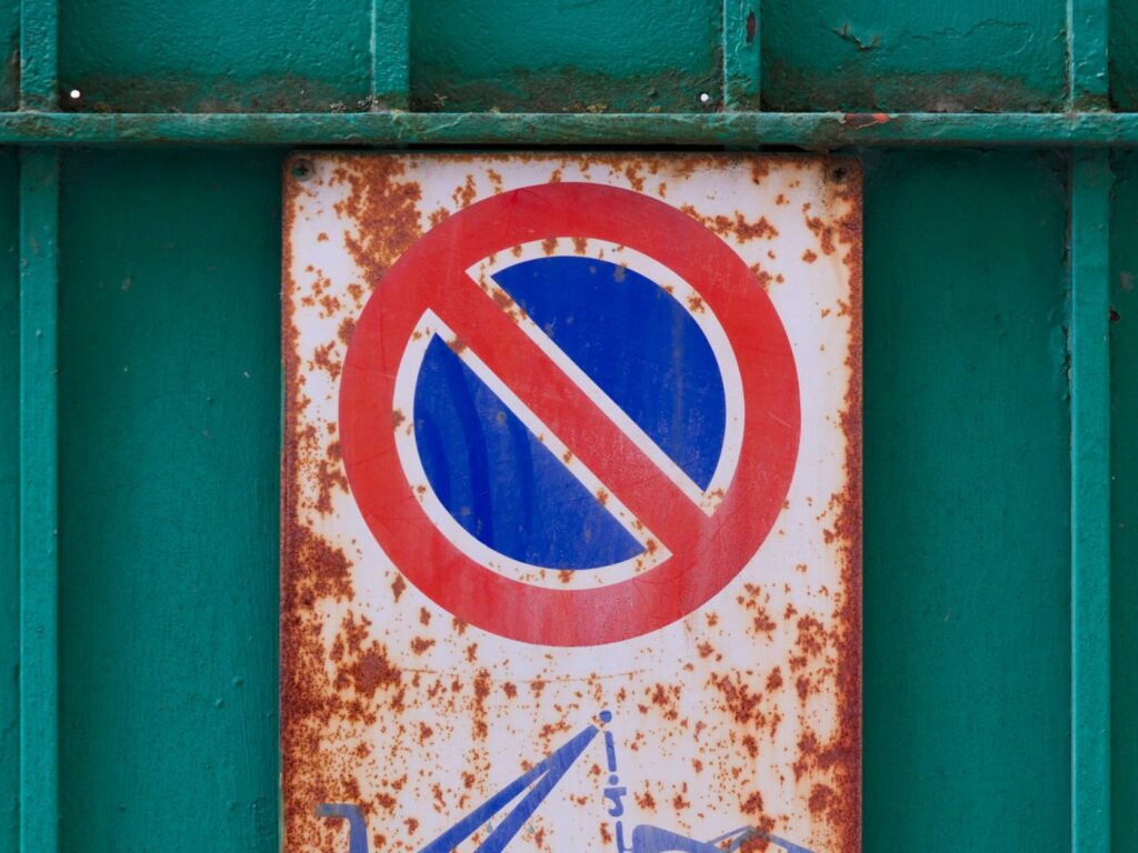 Heavily rusted metal no-parking sign mounted on a green painted metal wall