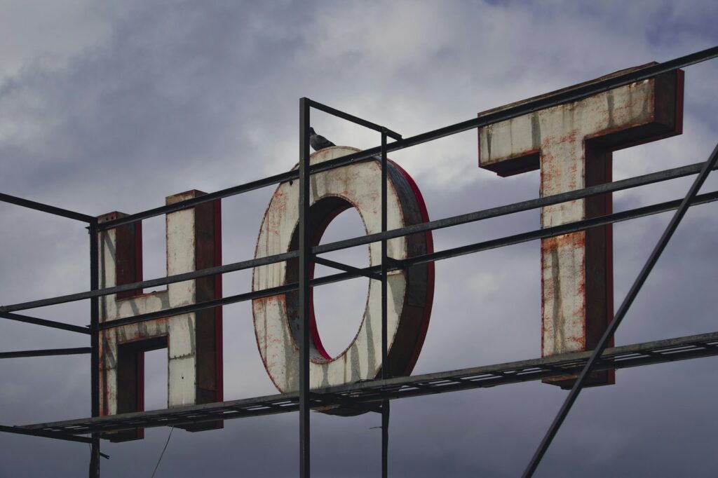 Large weathered metal letters on a steel frame against a cloudy sky, with worn and faded paint